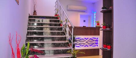 Una escalera de mármol con barandilla que lleva a una recepción con pared estampada y plantas en macetas.