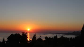 A sunset over a body of water with silhouettes of trees and distant buildings.