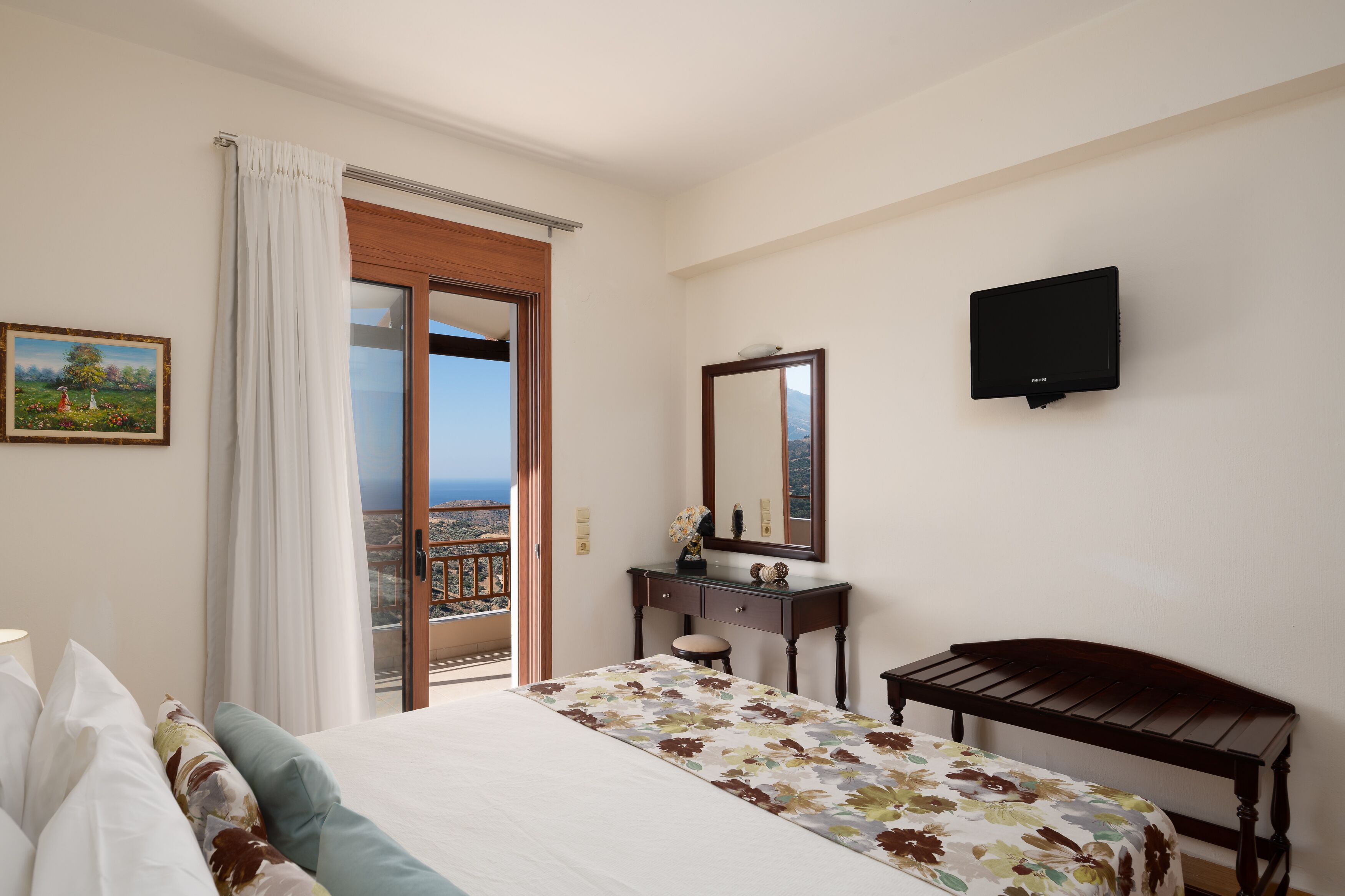 A hotel room with a bed, a desk, a mirror, a television, and a balcony with a view.