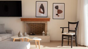 Un salon avec une cheminée, un canapé, une table basse et un fauteuil. Deux œuvres d’art encadrées sont accrochées au mur, au-dessus de la cheminée.