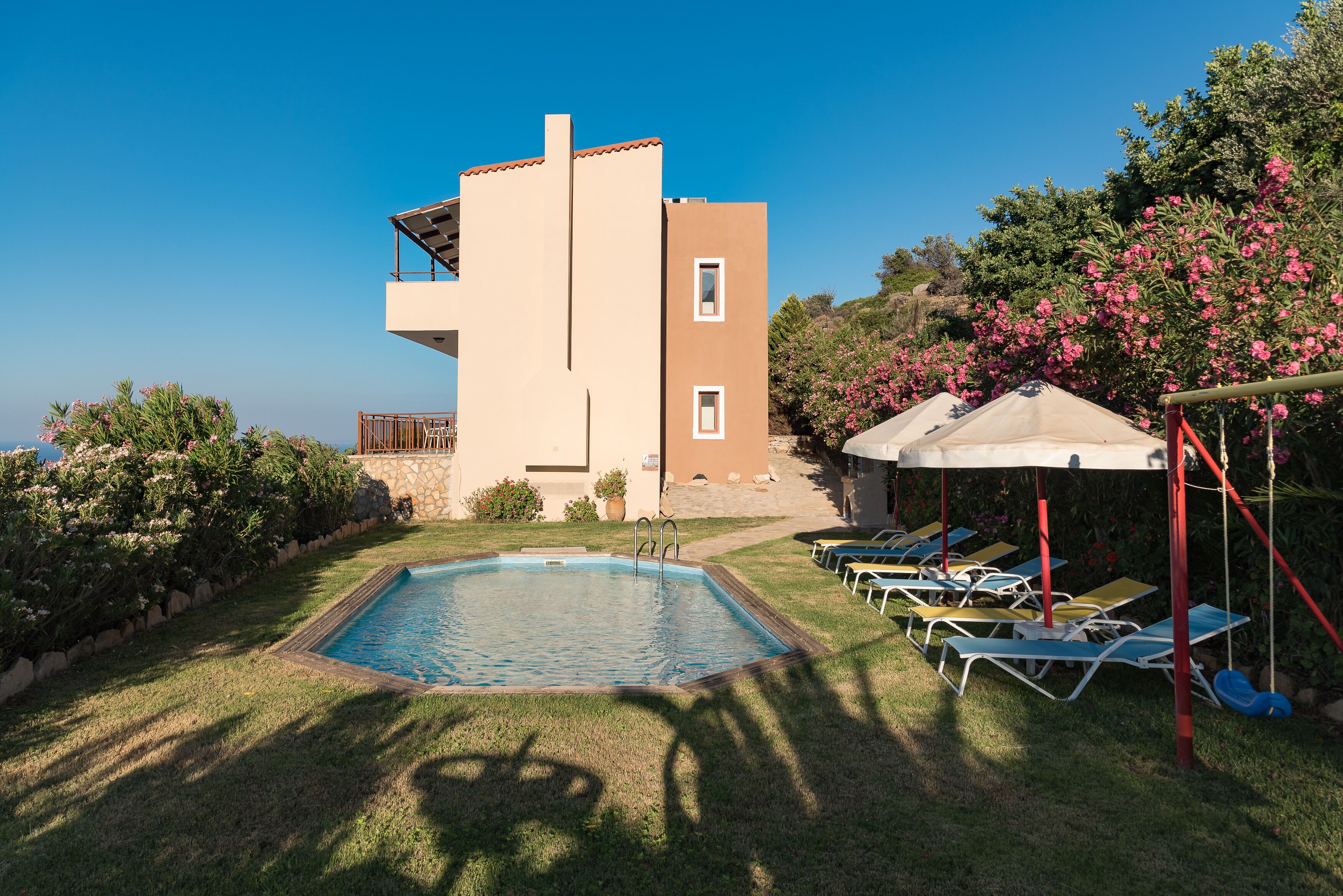 A pool area with a clear view of the pool, lounge chairs, and a building with a balcony.