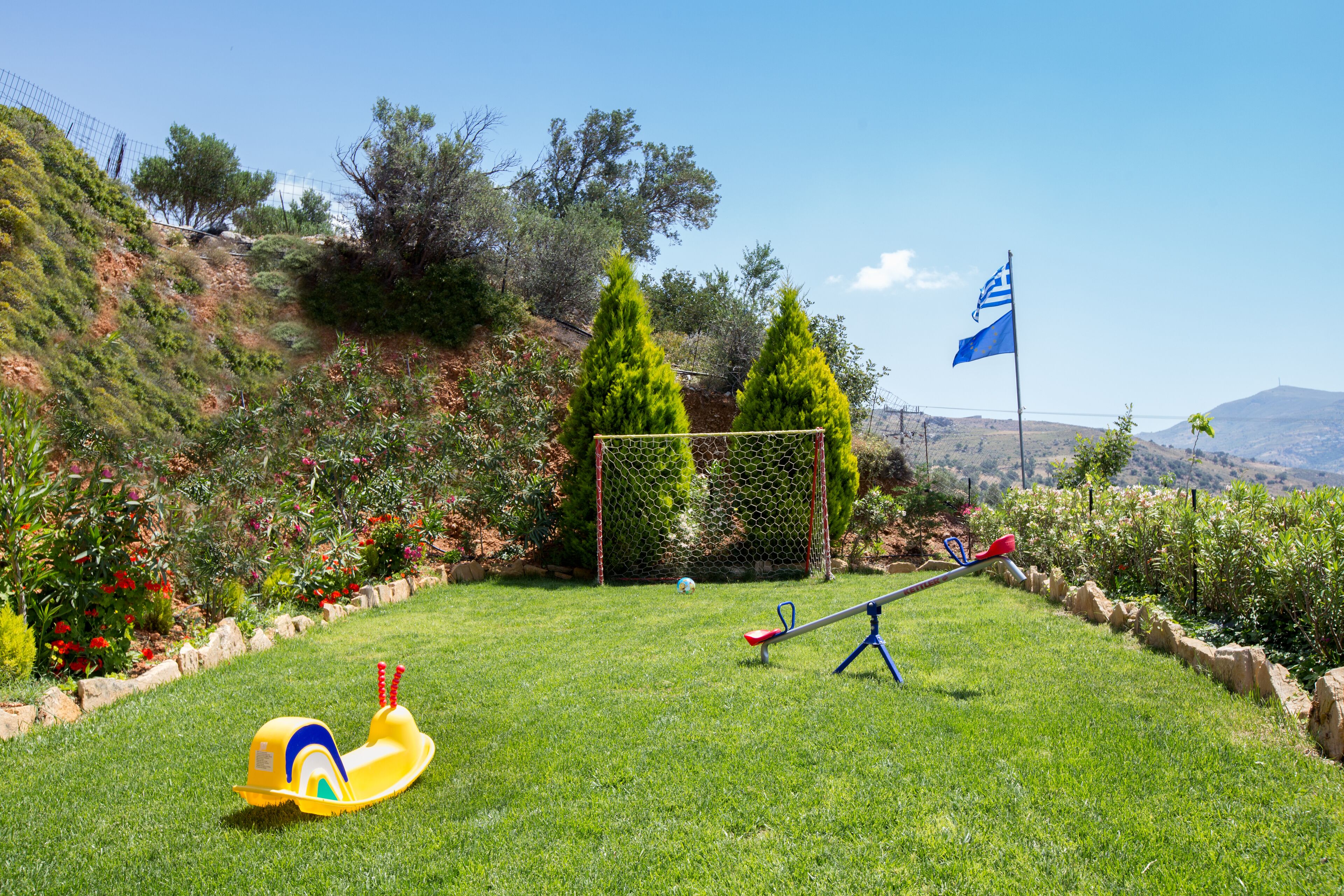 A grassy outdoor area with a seesaw, a yellow slide, and a flag.
