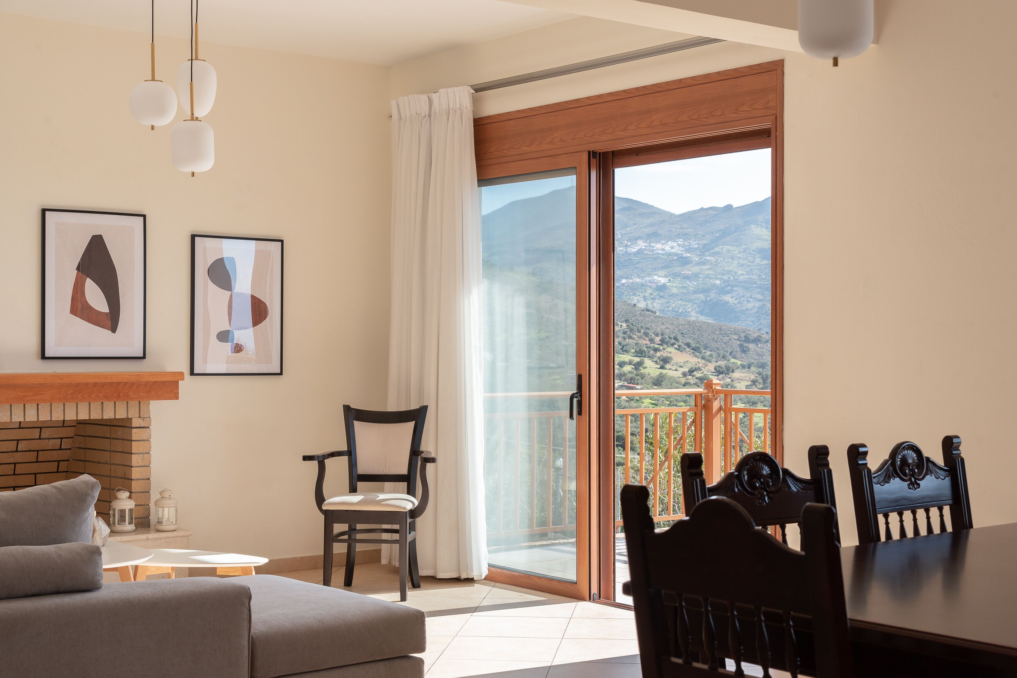 A living room with a fireplace, a dining table, chairs, a sofa, and a balcony with a mountain view.