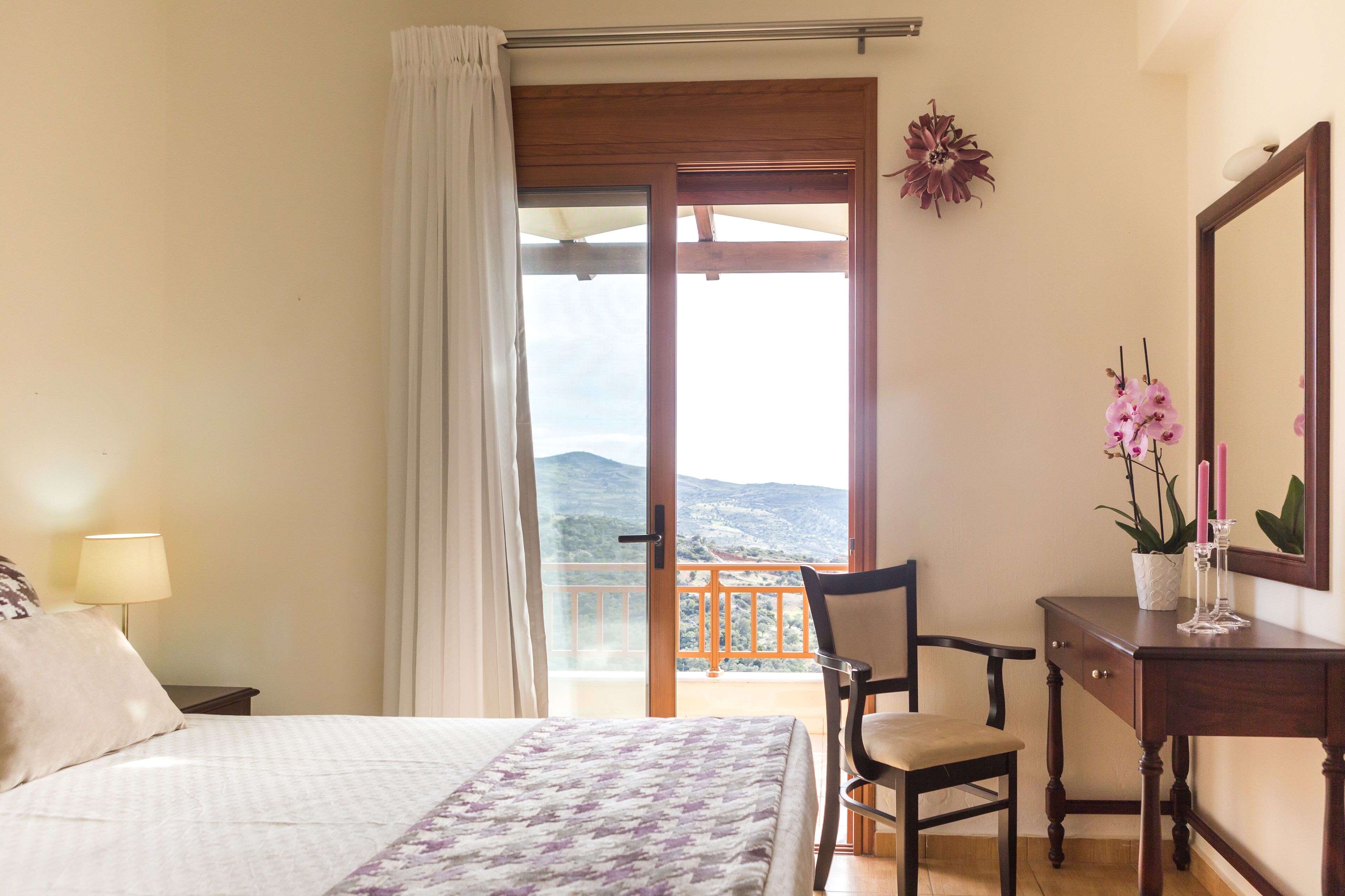 Una camera da letto con un letto, una sedia, un comodino, una cassettiera e un balcone con vista sulle montagne.