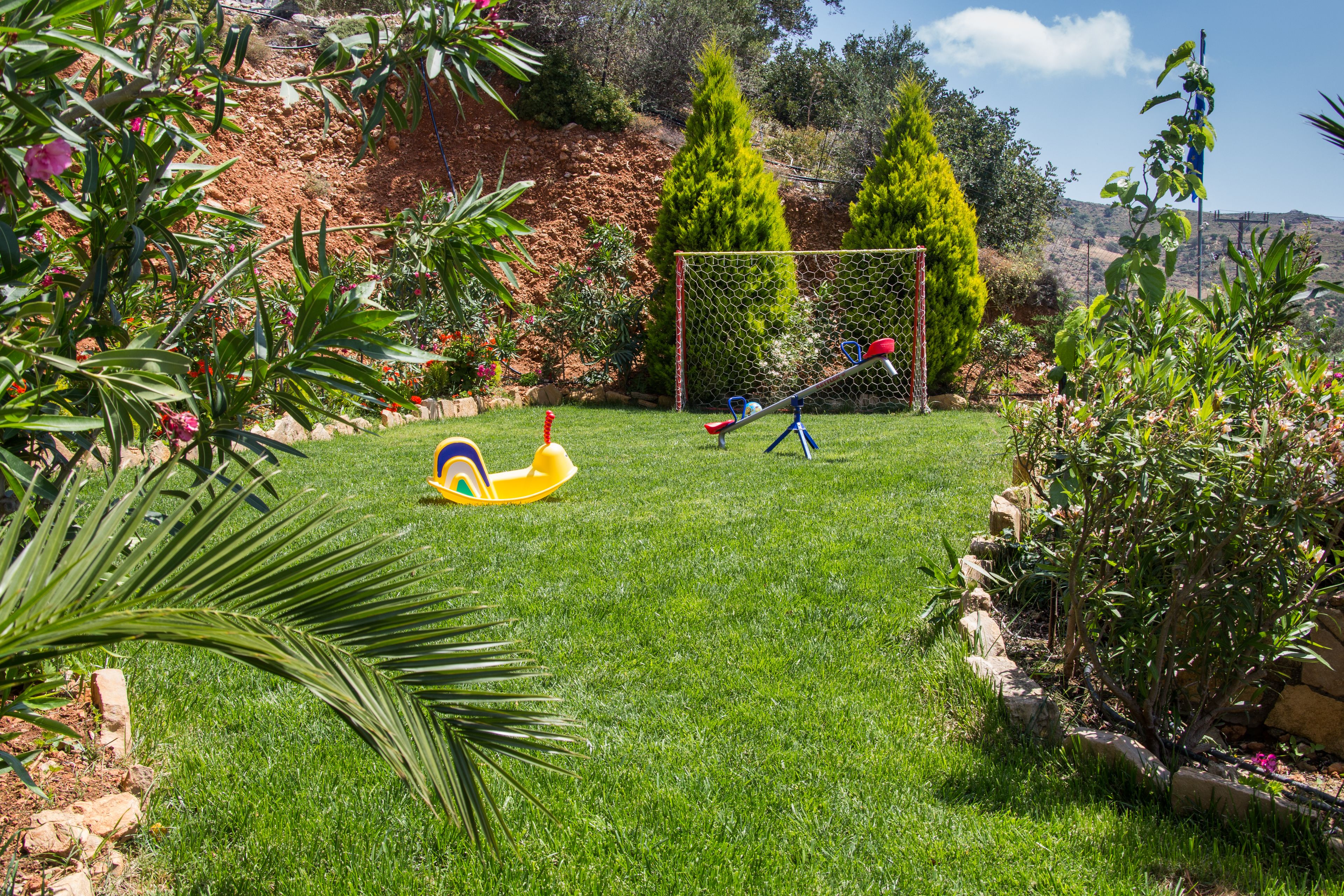 A well-maintained garden with a grassy lawn, a children's play area, and a variety of plants and trees.