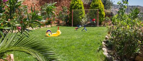 A well-maintained garden with a grassy lawn, a children's play area, and a variety of plants and trees.