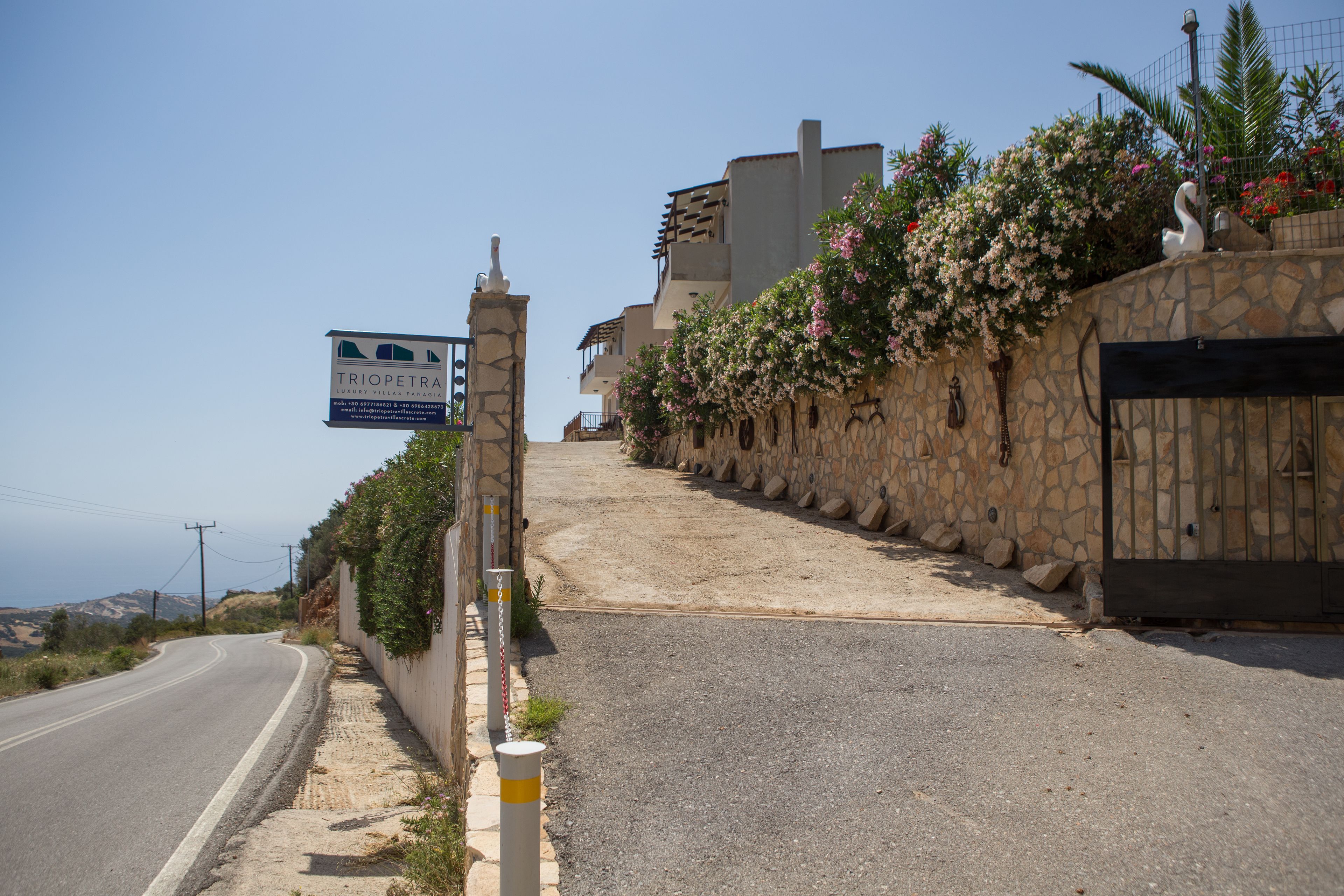 A stone wall with a gate, a sign for a hotel, and a road curving to the left.