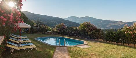 A swimming pool with a stone pathway leading to it, surrounded by grass and a view of mountains.