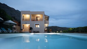 Un bâtiment moderne à deux étages, doté d’une piscine, d’un espace extérieur aménagé et offrant une vue sur un paysage montagneux.