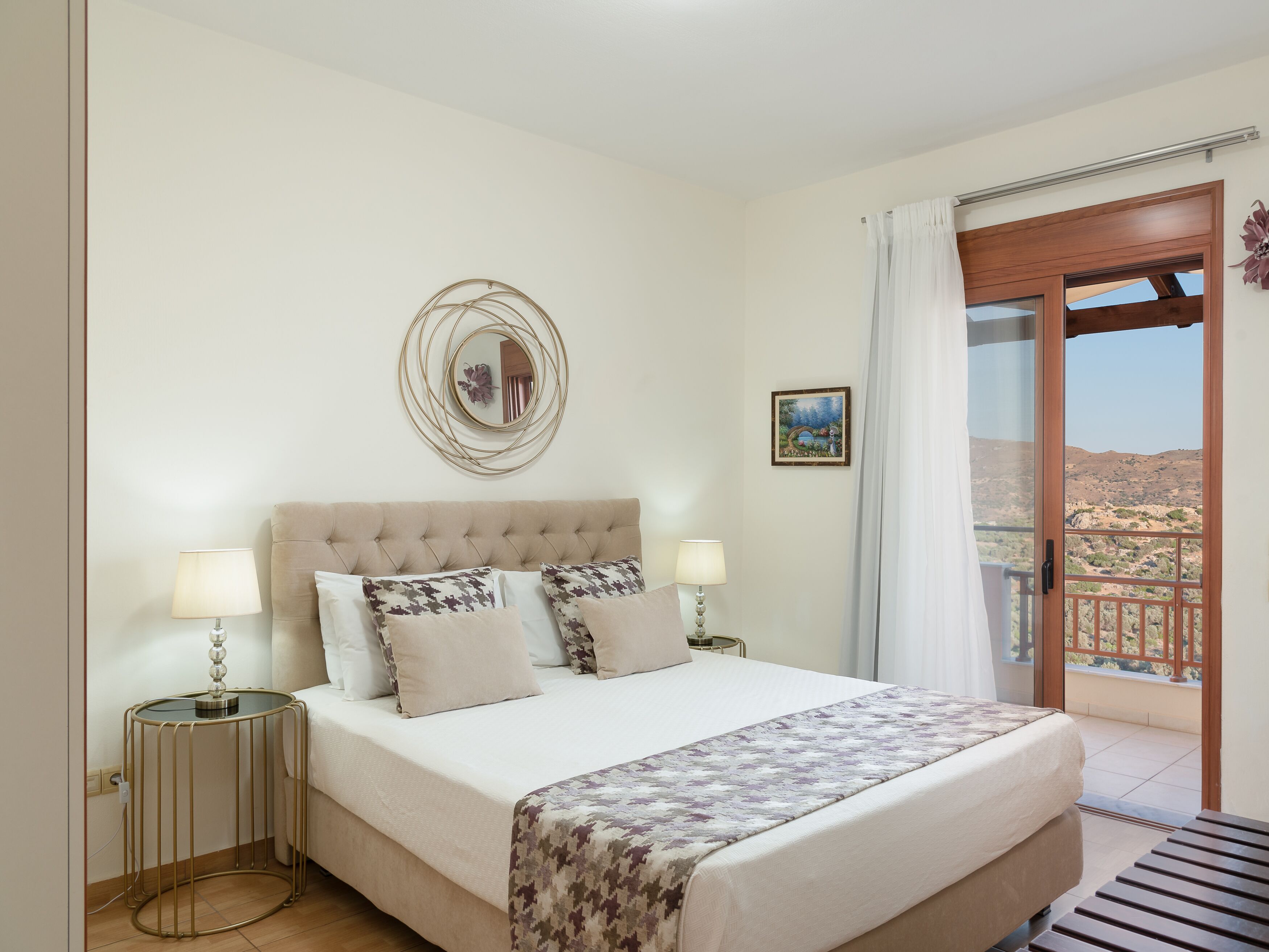 A bedroom with a bed, two bedside tables, a wall-mounted mirror, a picture, and a balcony with a view.