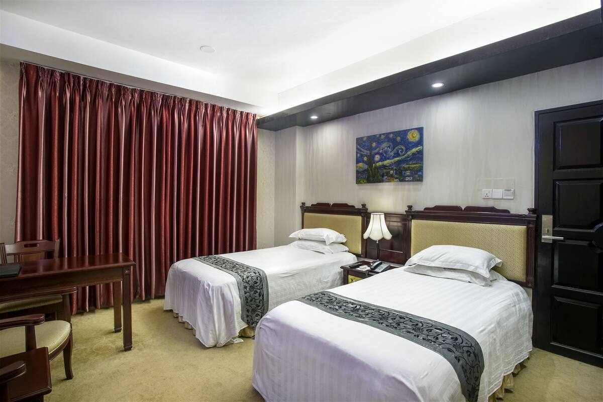 Una habitación de hotel con dos camas, un escritorio, una silla y un cuadro en la pared.