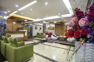 Un moderno vestíbulo de hotel con asientos verdes, un mostrador de recepción y un gran arreglo floral.
