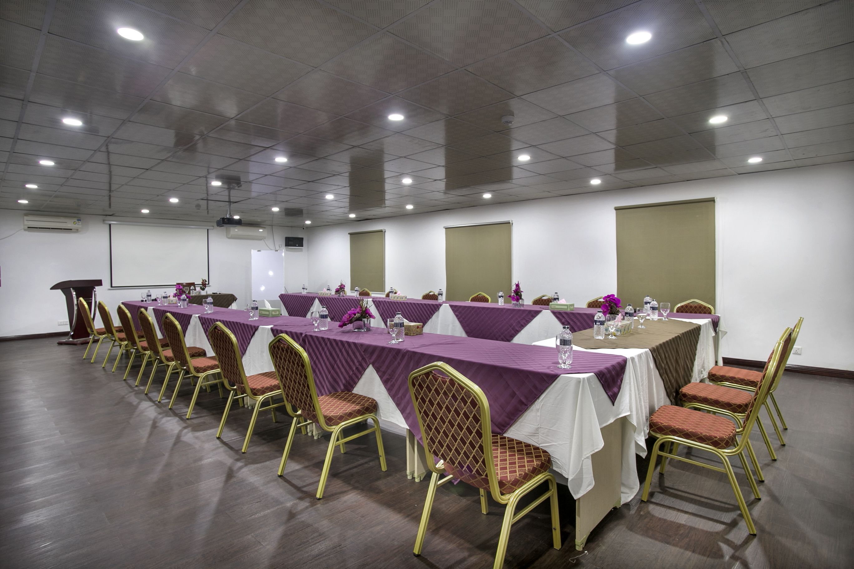 A conference room with long tables, chairs, and a projector screen.