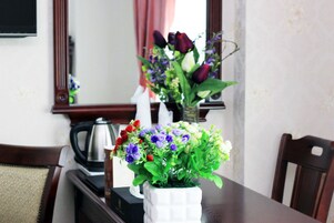 Una mesa de comedor con un jarrón blanco con flores, una cafetera negra y un holder blanco para servilletas.
