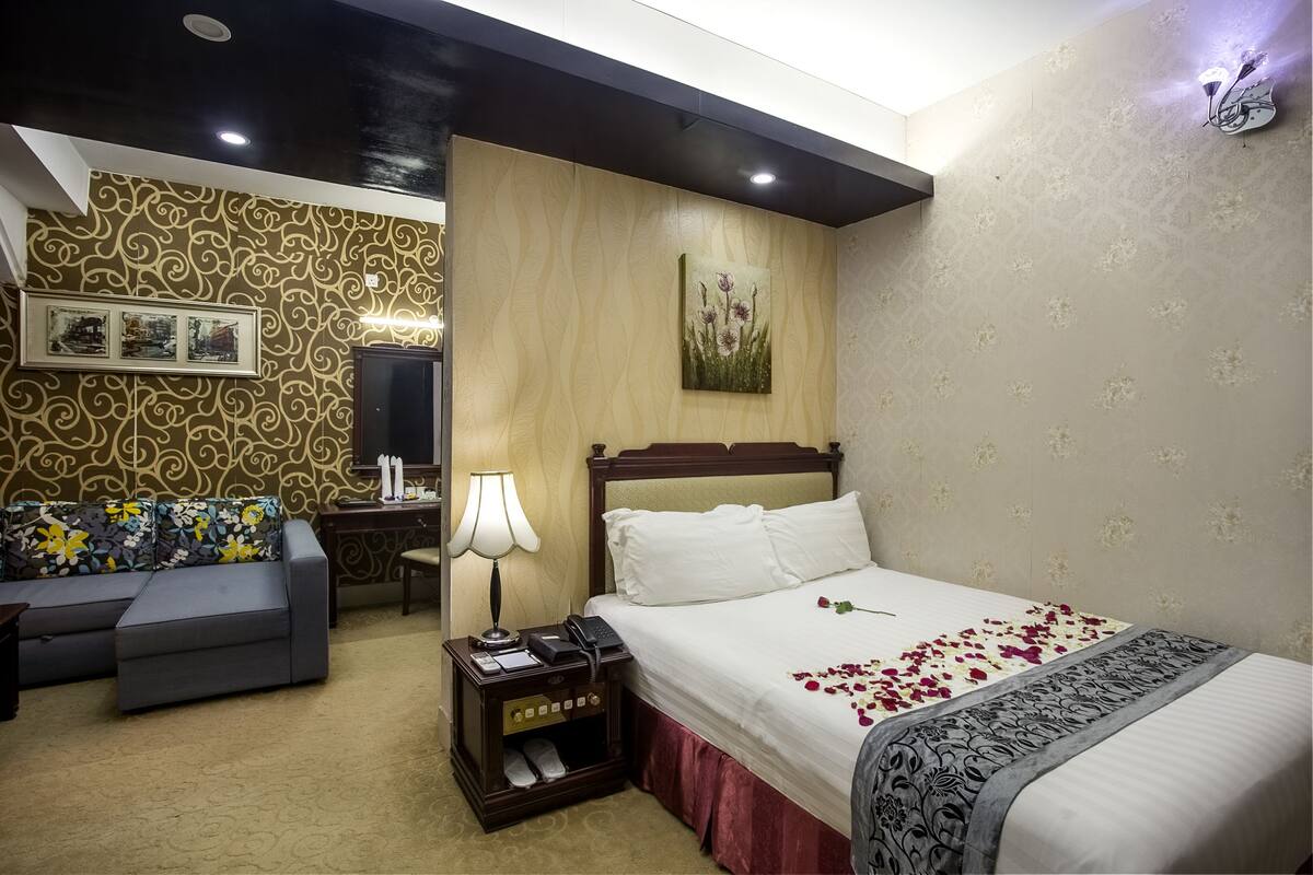 Una habitación de hotel con cama, sofá, mesita de noche con lámpara y un papel tapiz estampado.