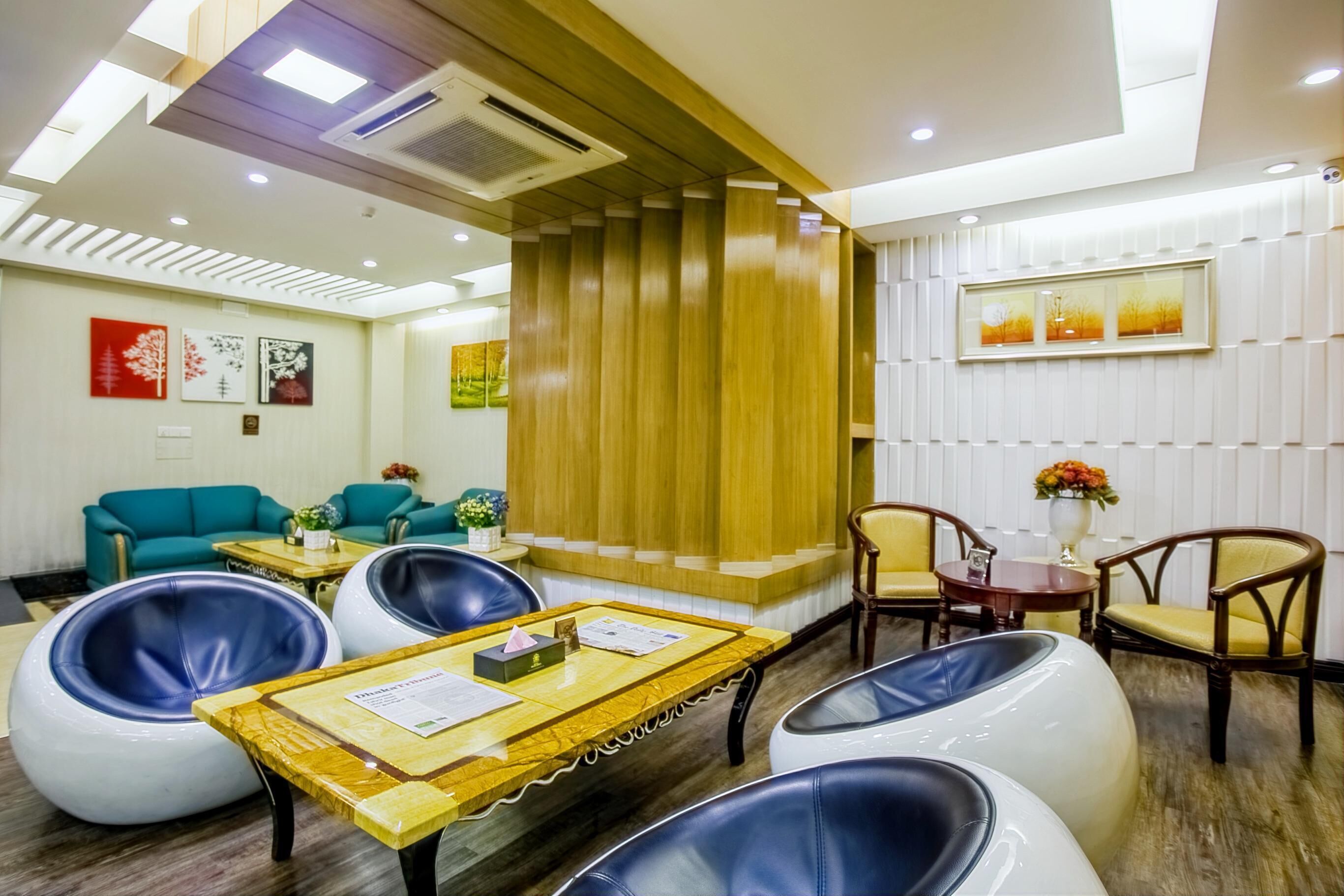 A modern hotel lobby with a teal sofa, round seating, a wooden reception desk, and framed artwork on the walls.