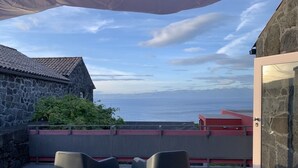 A balcony with two chairs, a stone building, and a view of the sea. - A Casa do Ouvidor (Sao Roque do Pico)
