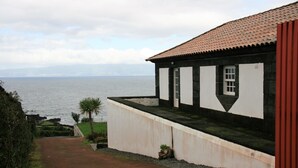 A coastal building with a view of the sea, a pathway leading to the entrance, and a small garden area. - A Casa do Ouvidor (Sao Roque do Pico)