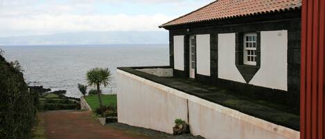 A coastal building with a view of the sea, a pathway leading to the entrance, and a small garden area.