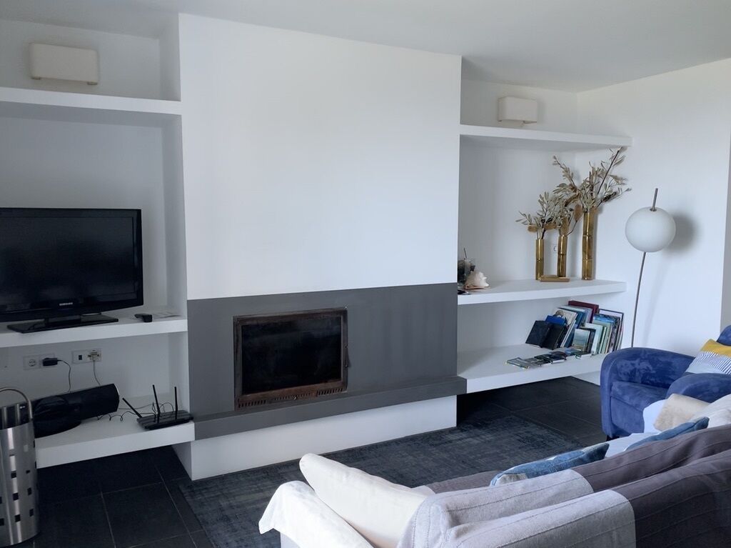A modern living room with a flat-screen TV, a fireplace, a bookshelf, and a blue sofa.