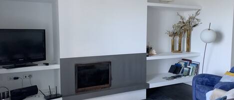 A modern living room with a flat-screen TV, a fireplace, a bookshelf, and a blue sofa.