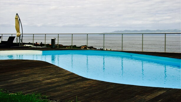 A swimming pool with a wooden deck, a yellow umbrella, and a view of the sea. - A Casa do Ouvidor (Sao Roque do Pico)