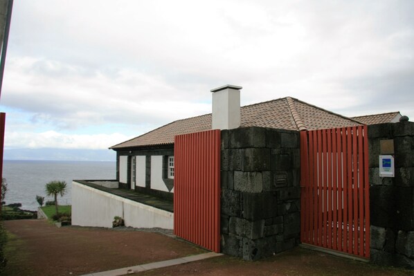 A coastal building with a tiled roof, a stone wall, and a red gate.