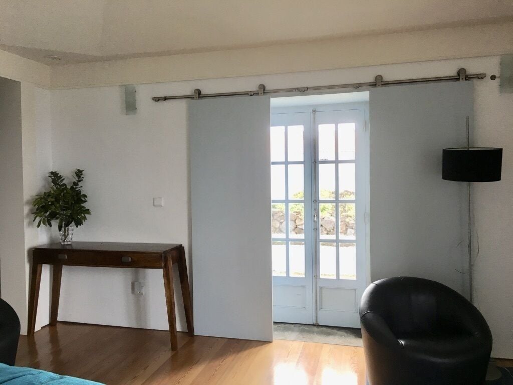 Une pièce avec un plancher en bois, une petite table sur laquelle est posée une plante, une chaise noire et une porte coulissante donnant sur un balcon.