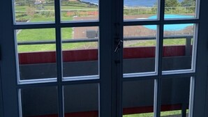 A view through a window with multiple panes, overlooking a coastal landscape with a clear sky, a body of water, and a swimming pool. - A Casa do Ouvidor (Sao Roque do Pico)