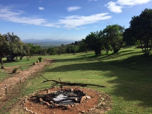 A circular fire pit surrounded by a dirt path, with trees and a clear sky in the background.