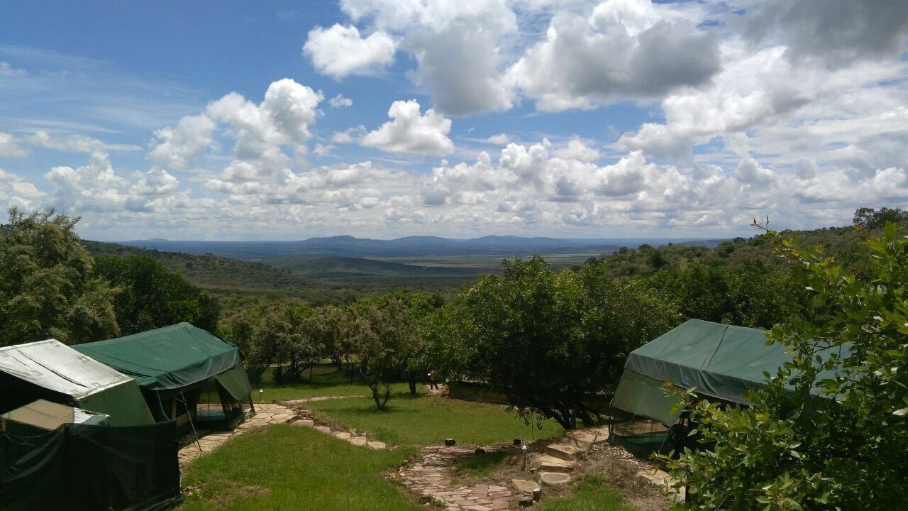 A campsite with tents, a stone pathway, and a view of distant mountains under a partly cloudy sky.