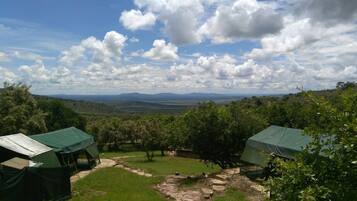 A campsite with tents, a stone pathway, and a view of distant mountains under a partly cloudy sky.