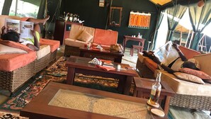 A tented accommodation with wicker furniture, a central table, and a view of the outdoors.