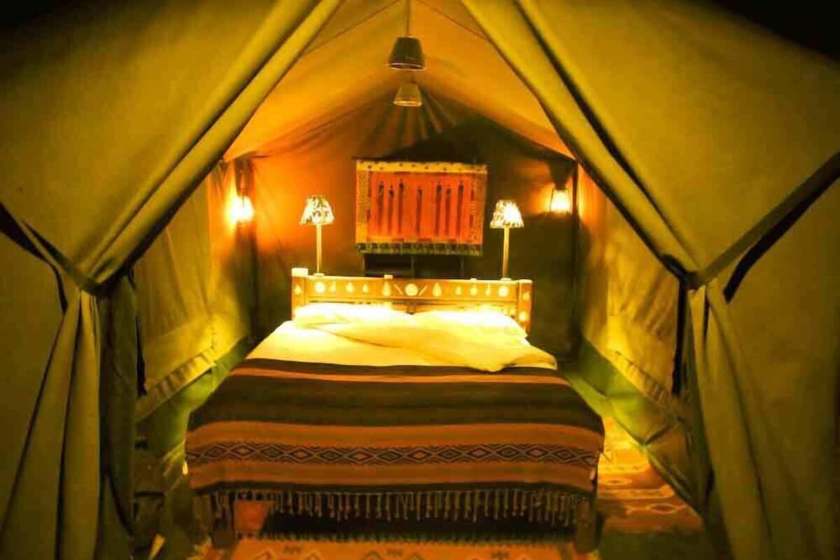 Ein Zelt mit einem Bett, zwei Lampen und einer Hängelampe.