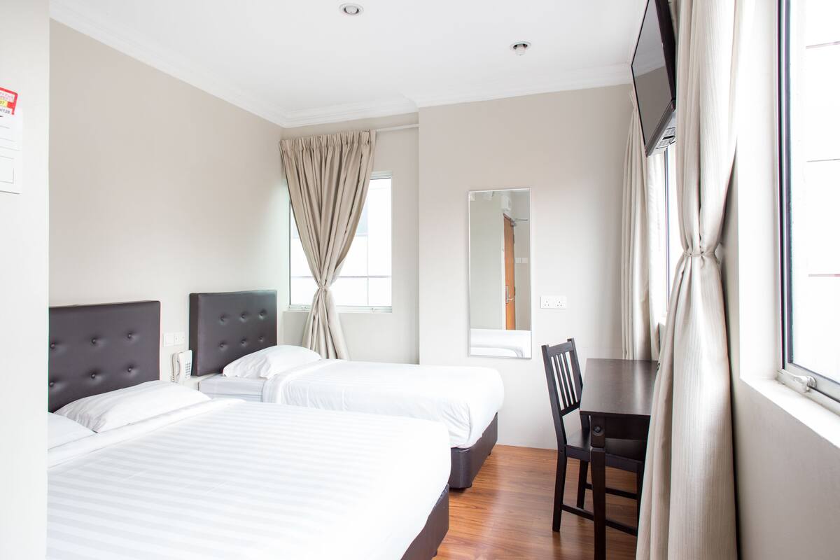 A hotel room with two beds, a desk, a chair, a TV, and a window with curtains.