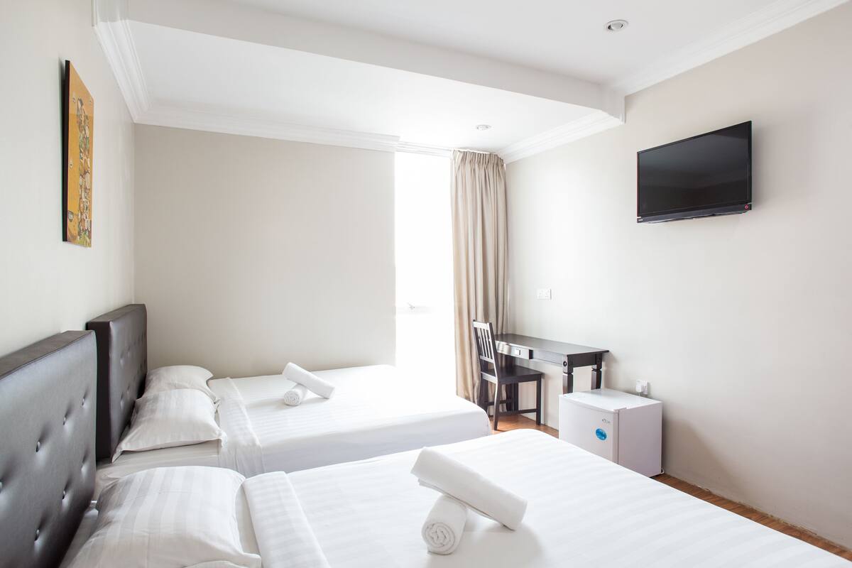 A hotel room with two beds, a desk, a chair, a TV, and a window with curtains.
