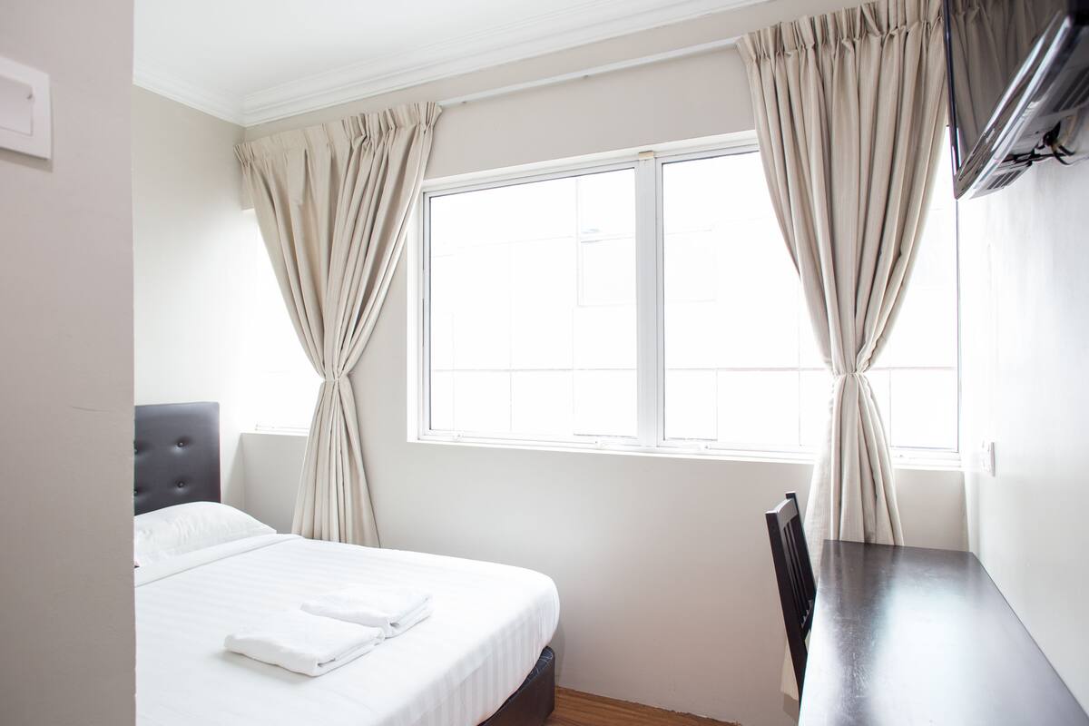 A hotel room with a bed, a desk, and a window with curtains.