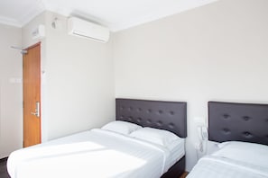Una camera d'albergo con due letti, una porta in legno, un condizionatore d'aria e un telefono appeso al muro.