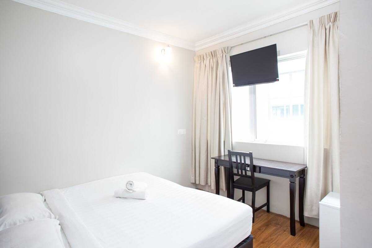 A hotel room with a bed, a desk, a chair, and a TV mounted on the wall.