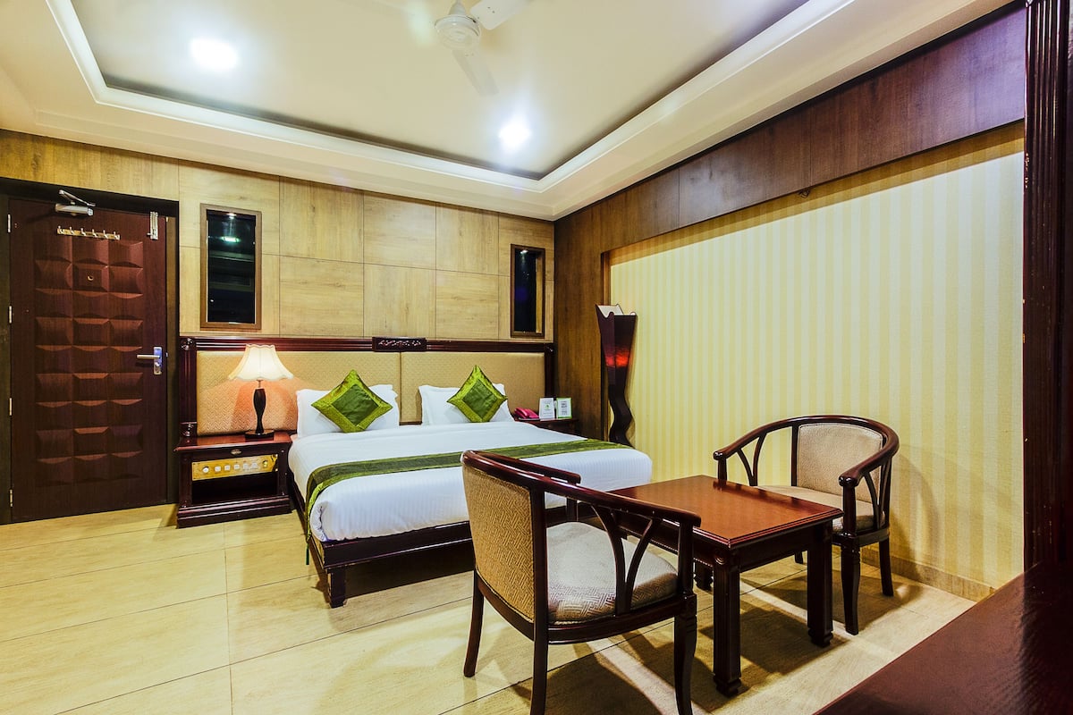 A hotel room with a bed, bedside table, lamp, two chairs, and a small table.