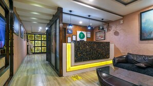 A reception area with a wooden reception desk, a black leather sofa, and a glass coffee table. - Treebo Shivani (Indore)
