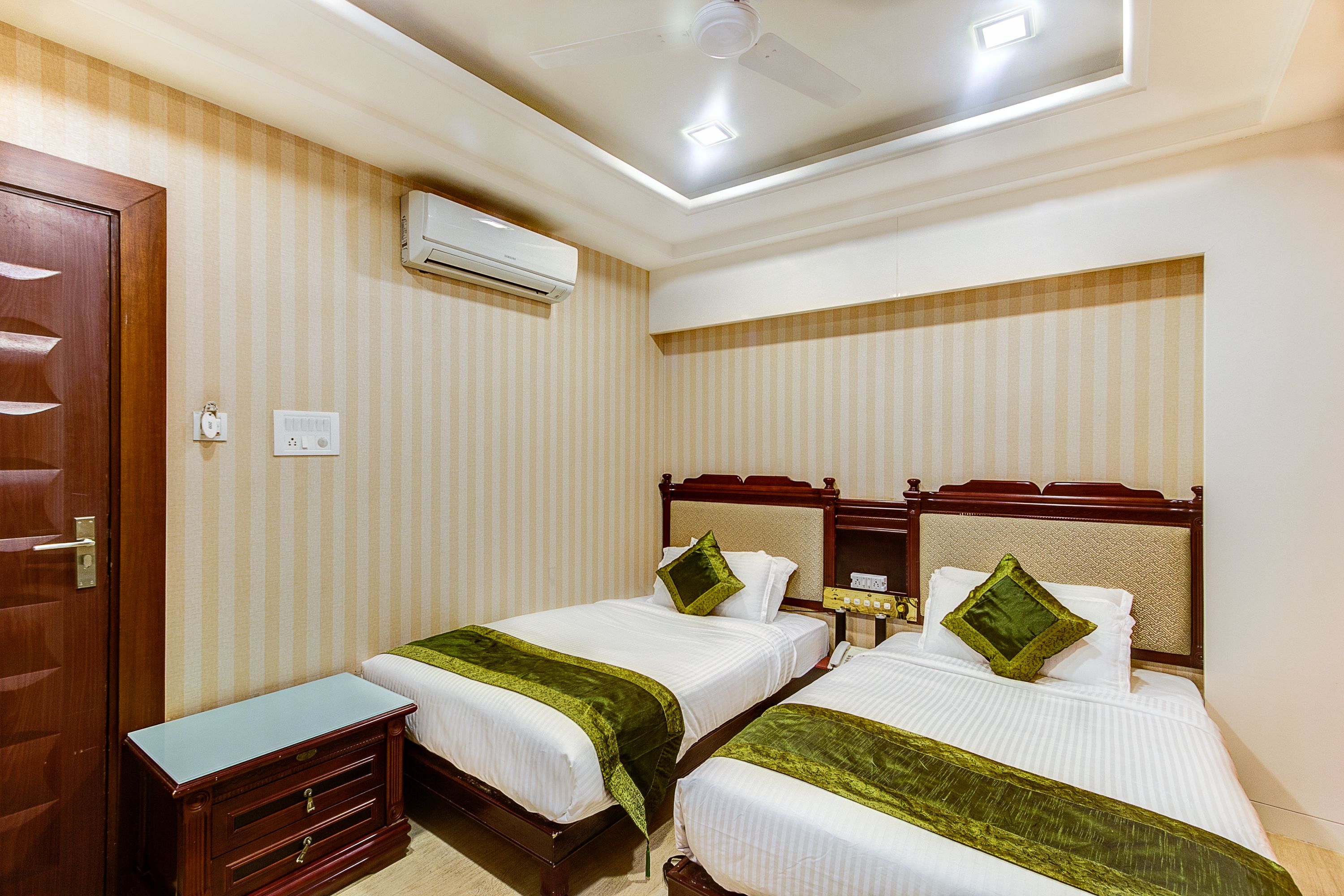 Habitación de hotel con dos camas, un aparador de madera, un equipo de aire acondicionado y un ventilador de techo.