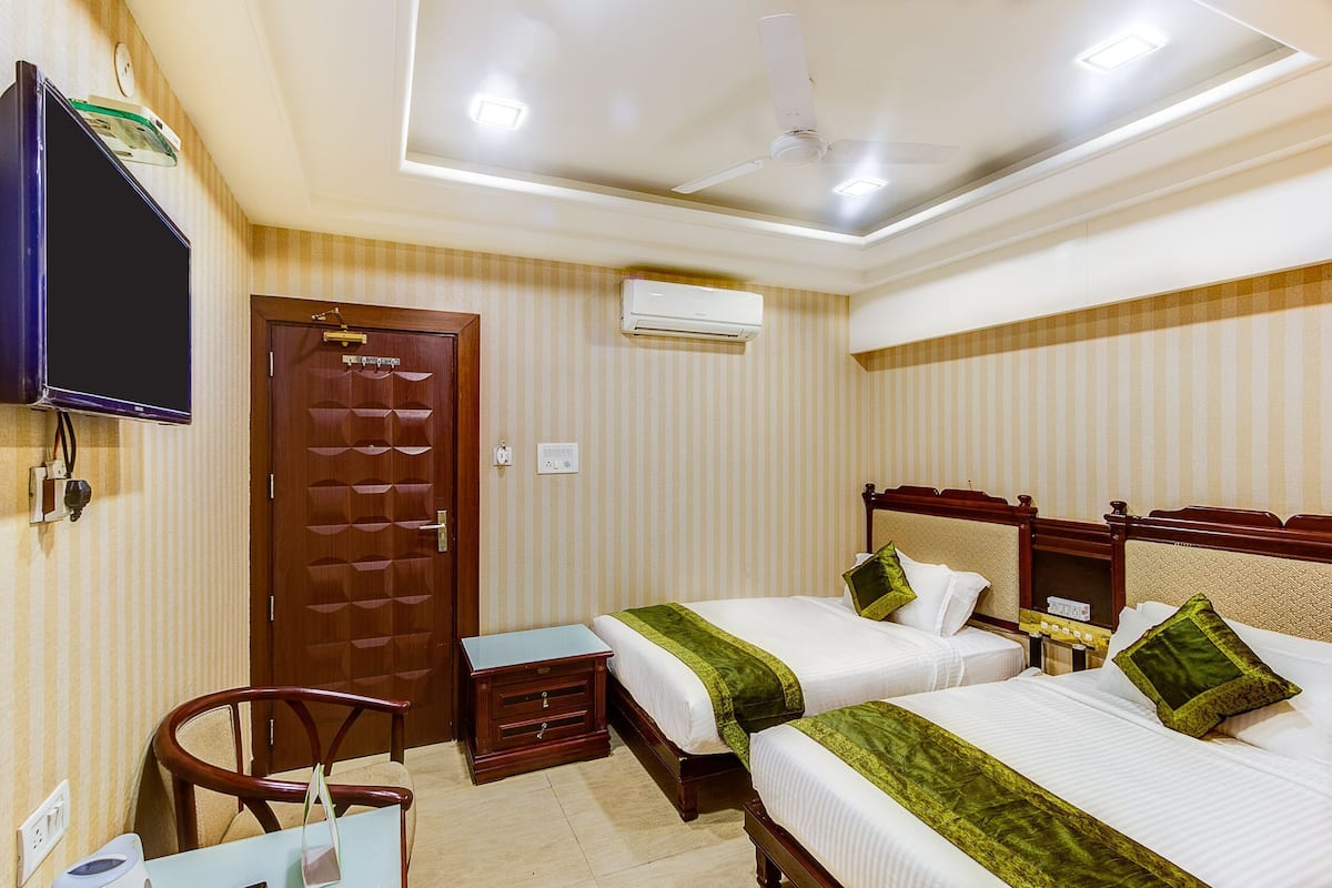 A hotel room with two beds, a desk, a chair, a television, and an air conditioning unit.