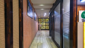A hallway with a tiled floor, wooden paneling, and a glass door with a 'T' logo. - Treebo Shivani (Indore)