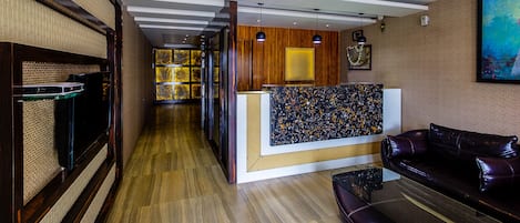Un vestíbulo de hotel con mostrador de recepción, un sofá de cuero, paneles de madera y un ventilador de techo.