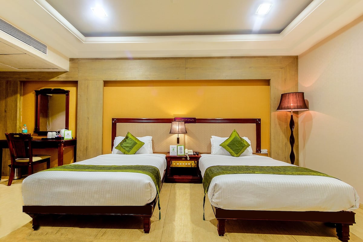 A hotel room with two beds, a desk, a chair, a lamp, and a telephone.
