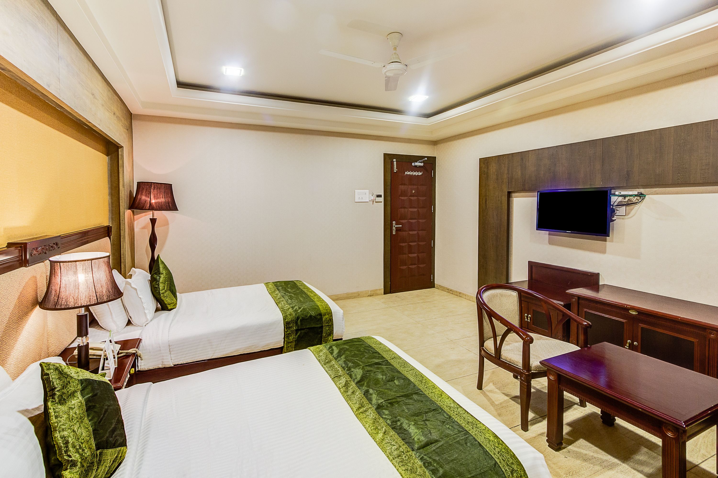 Une chambre d’hôtel avec deux lits, un bureau, une chaise, une télévision et une porte.