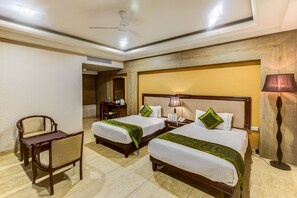 A hotel room with two beds, a desk, a chair, and a lamp. - Treebo Shivani (Indore)