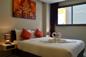 A neatly made bed with two swan-shaped towels, a painting on the wall, and a window with curtains. - C-View Boutique (Pattaya)