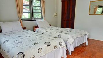 A room with two beds, each with a sun-patterned bedspread, a window with curtains, a wooden door, and a mirror on the wall.